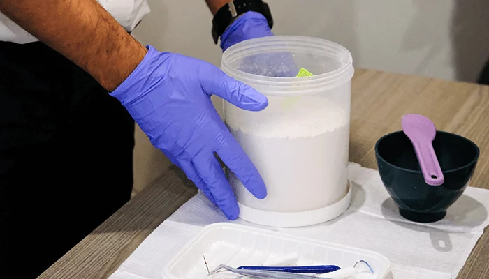 A dental prosthetist holds the impressions mixture container