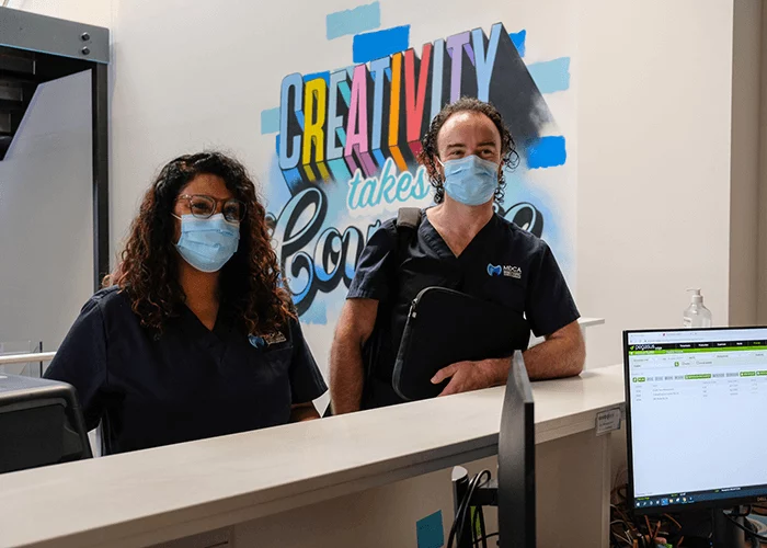 A dentist and dental assistant greet reception staff