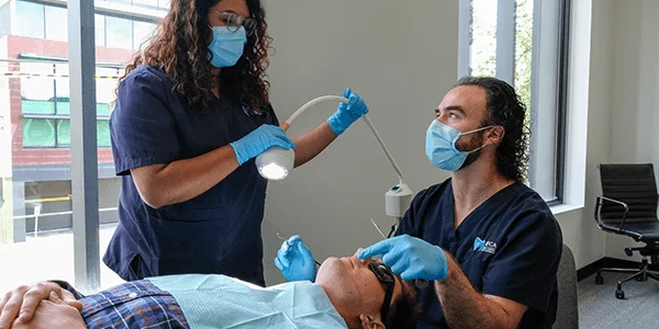 A dentist and dental assistant work with a young professional in their office